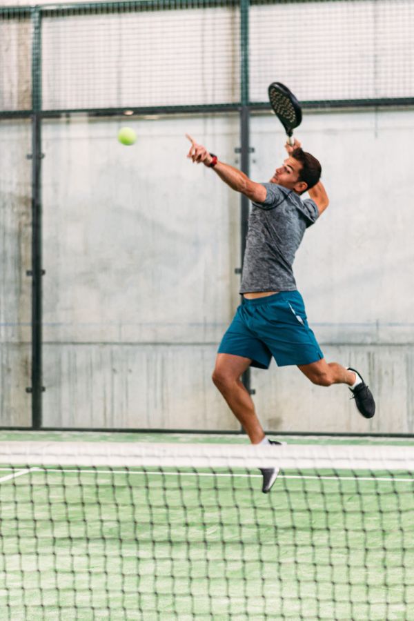 A man in athletic wear jumps to hit a tennis ball with a racket on an indoor court.